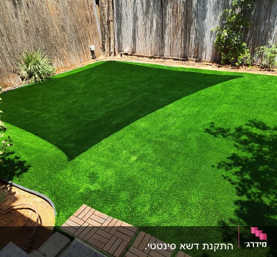דשא סינטטי בגינה עם גדר עץ וצמחים